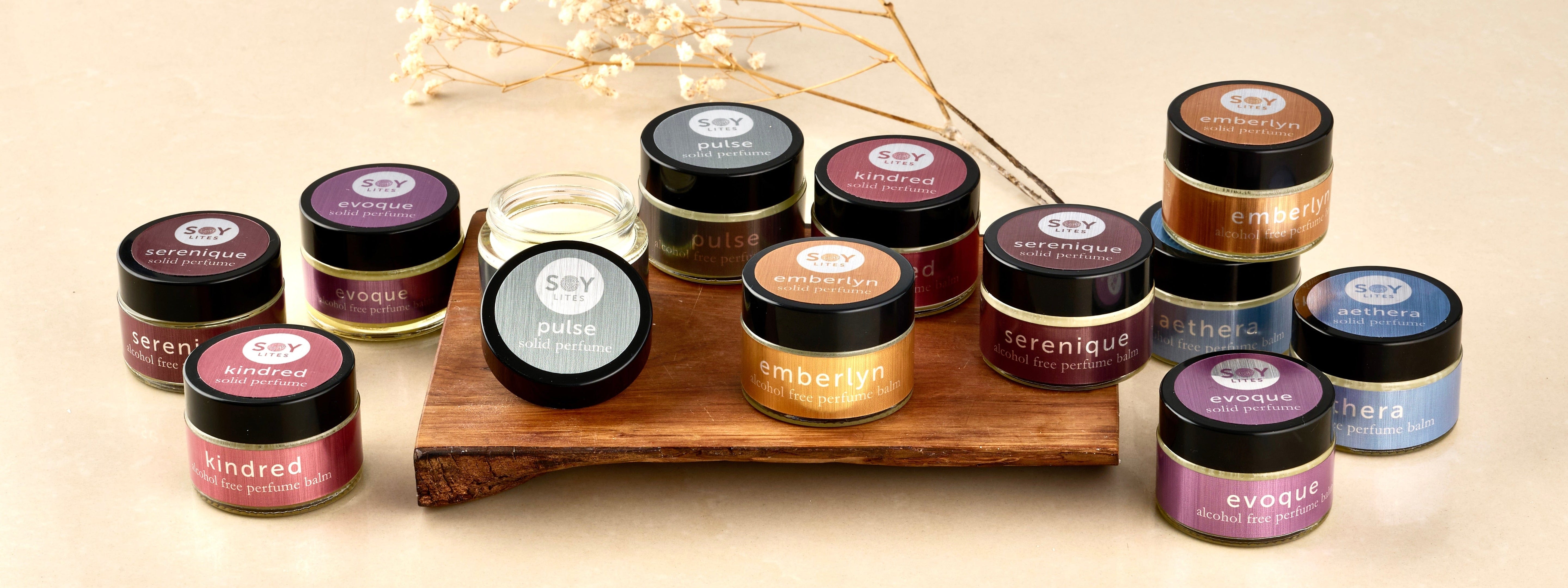 Collection of small jars of solid perfumes with labels on a wooden stand against a neutral background